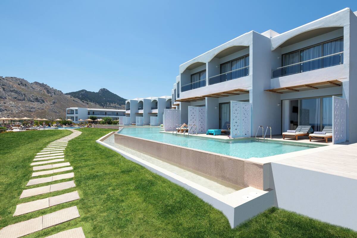 A modern hotel with a pool, outdoor seating, and a mountainous backdrop.