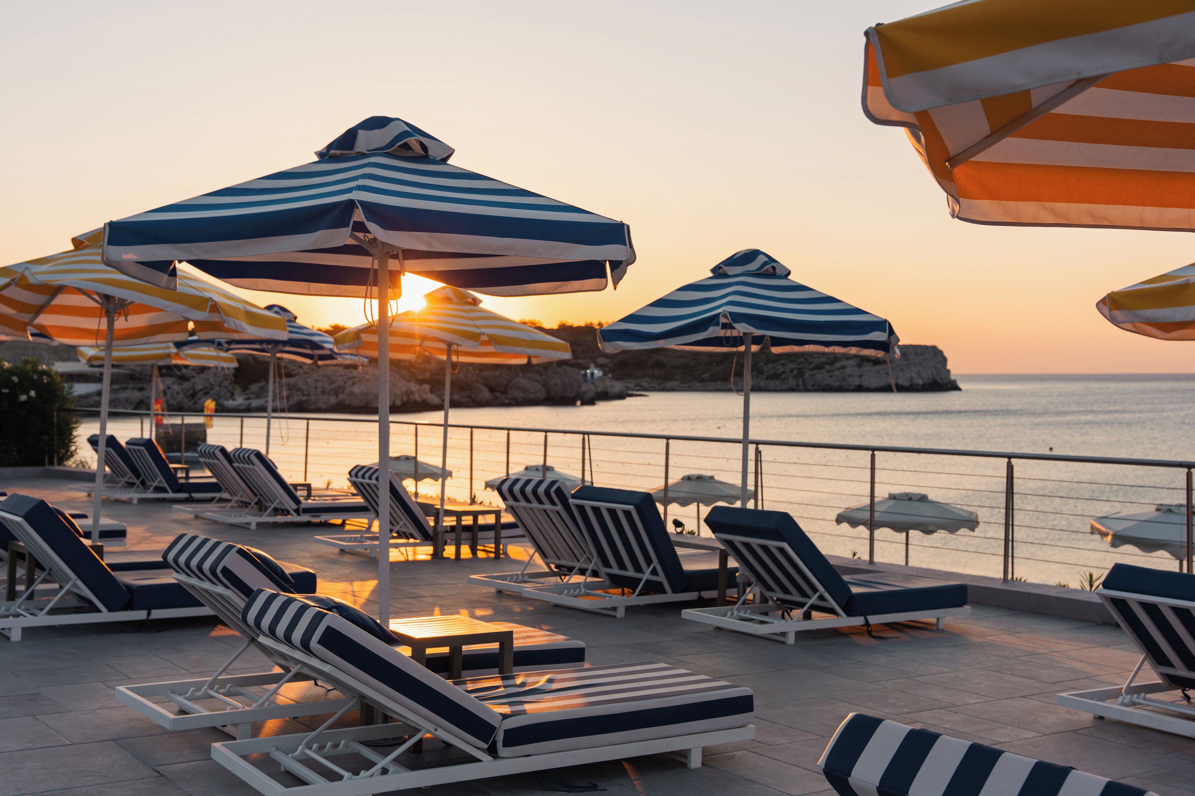 Een terras aan het strand met gestreepte parasols en comfortabele ligbedden.