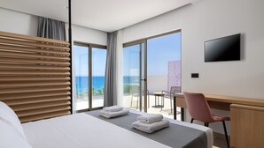A hotel room with a bed, a desk, a chair, a TV, and a balcony with a view of the sea.