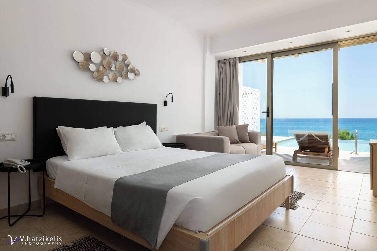 A modern bedroom with a large bed, a sofa, and a view of the sea.