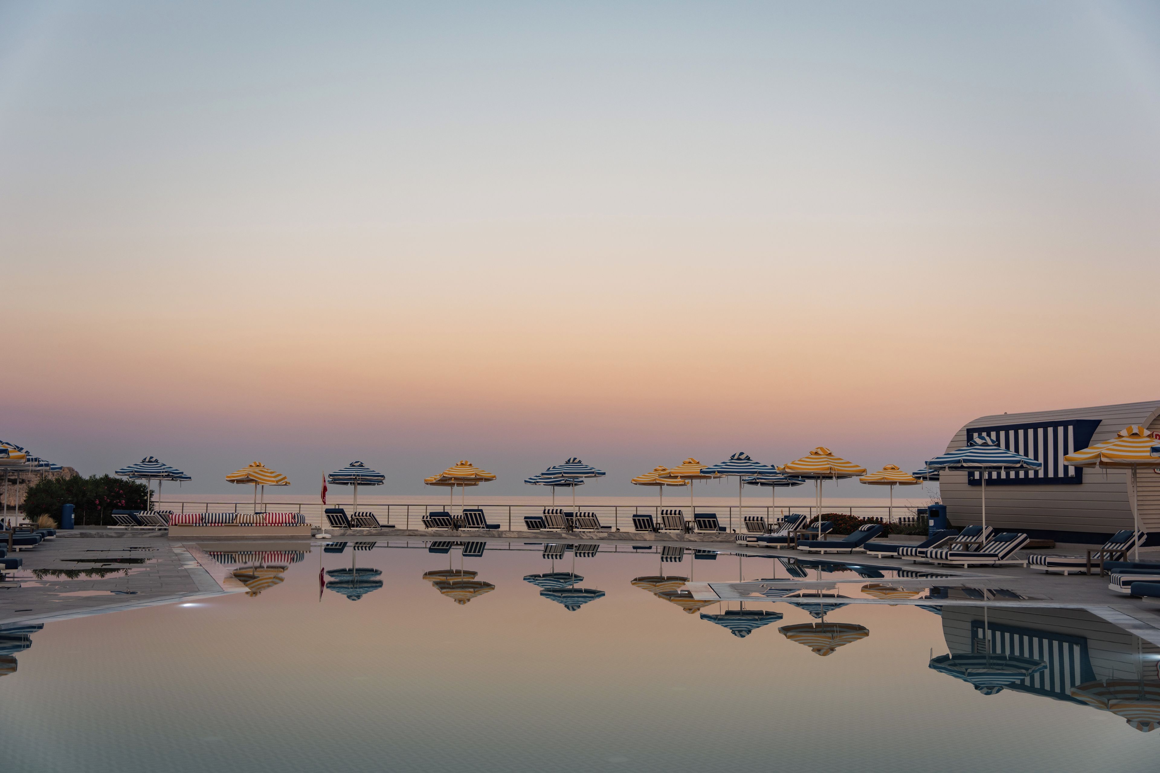 Un espace aménagé au bord de la piscine, avec des chaises longues et des parasols, dont le reflet se mire dans l’eau.