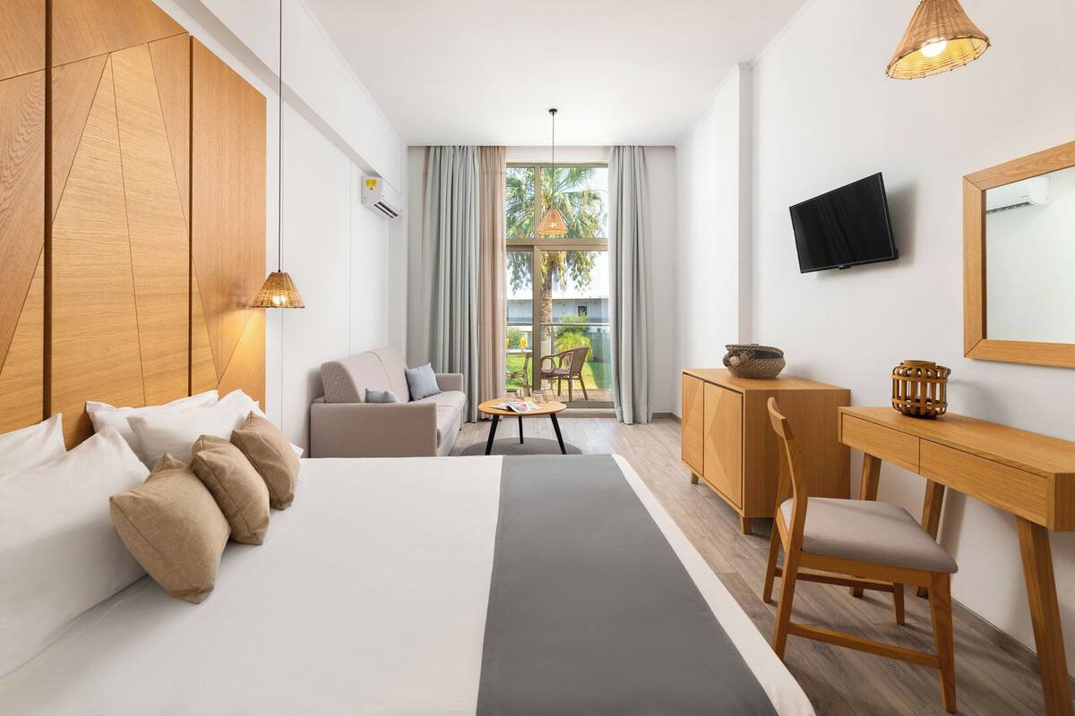 A modern hotel room with a large bed, a sofa, a desk, and a TV.
