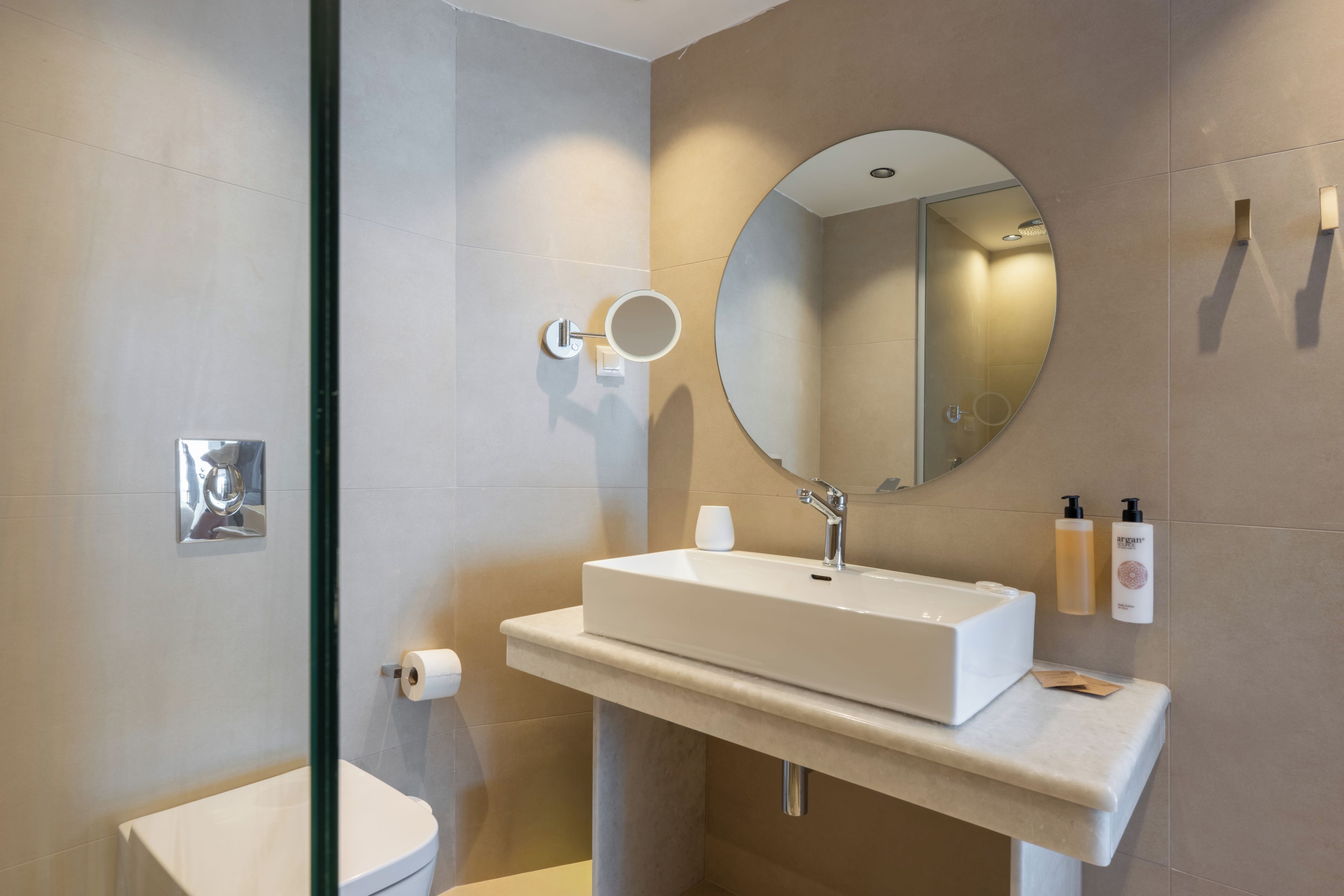 A modern bathroom with a white sink, a round mirror, and a toilet.