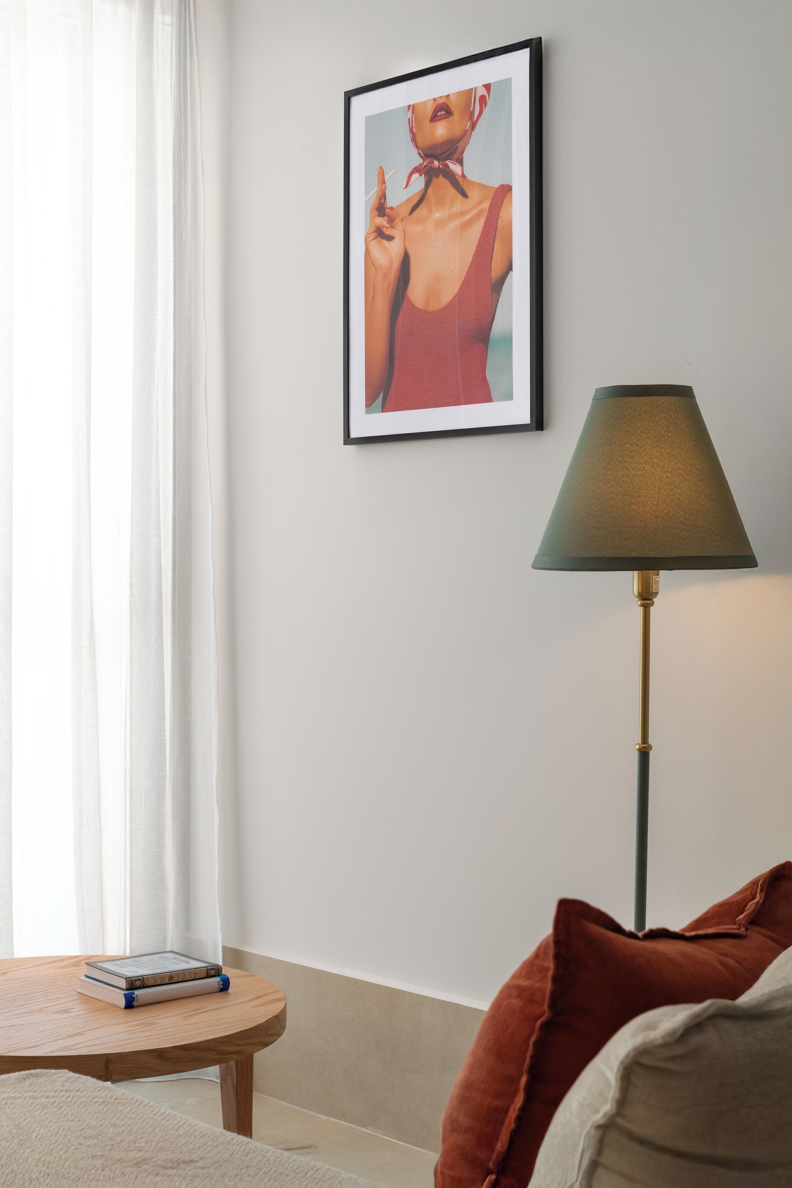 A room with a round wooden table, a framed picture on the wall, a floor lamp, and a couch with pillows.