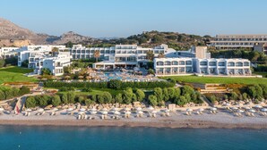 A resort with multiple white buildings, a central pool, and a beach area with umbrellas.
