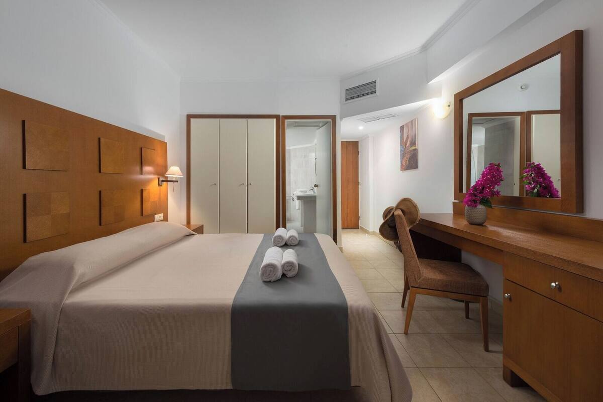 A hotel room with a bed, a desk, a chair, a mirror, and a bathroom visible through an open door.