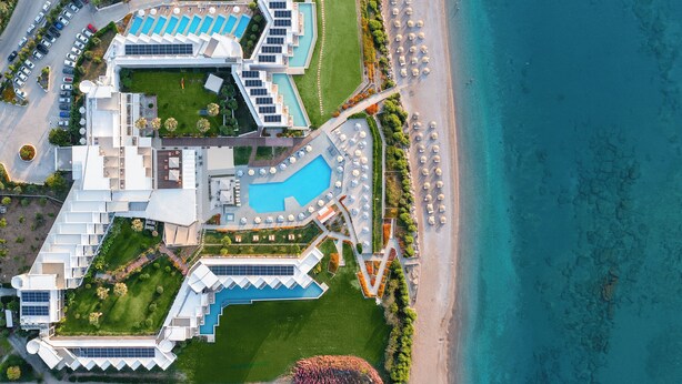 An aerial view of a resort with multiple swimming pools, a beach area, and a parking lot.