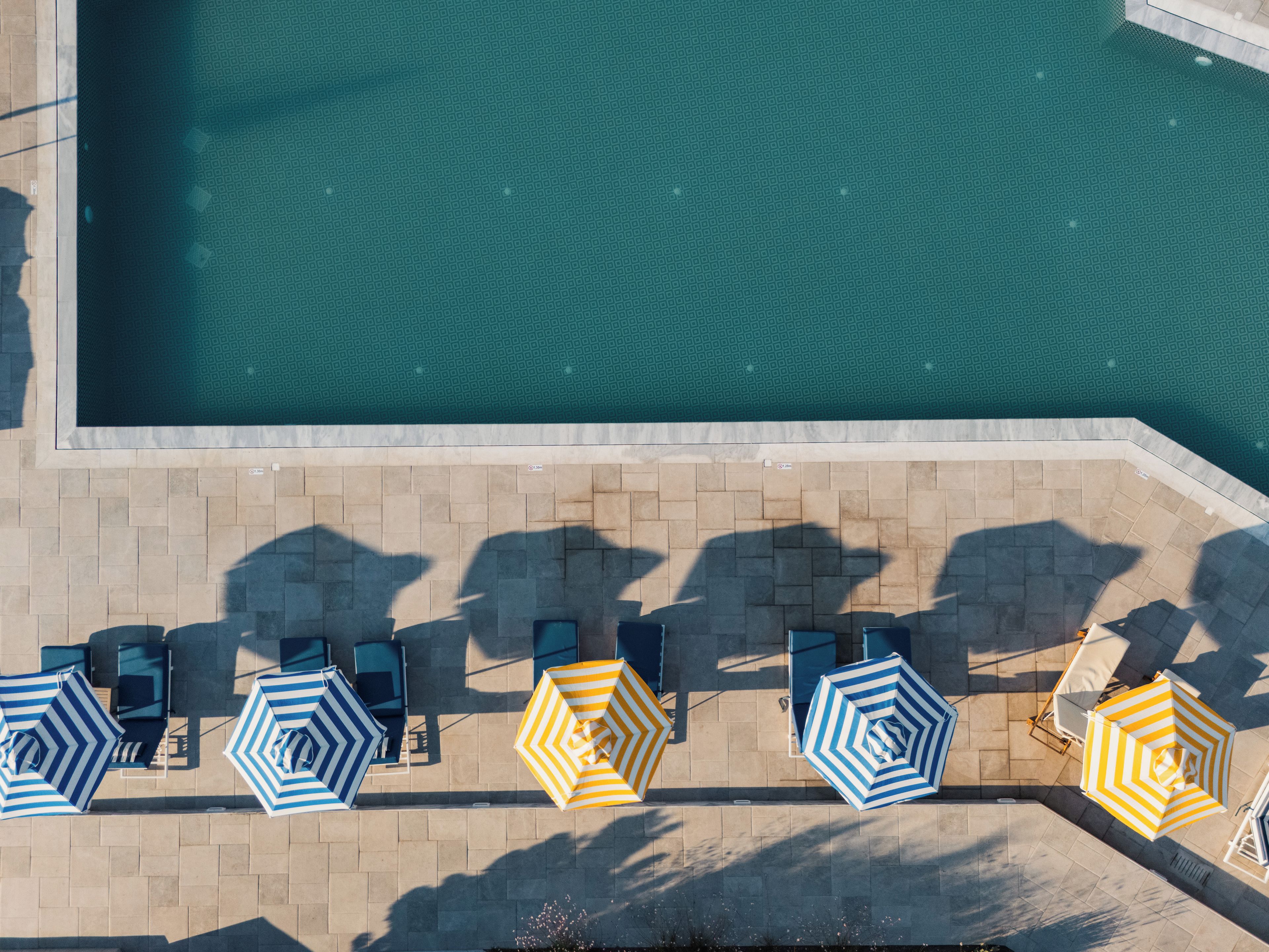 Vista aérea de una piscina con plataforma de azulejos y sombrillas.