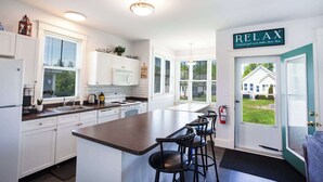 A modern kitchen with white cabinets, a large island with bar stools, and a 'RELAX' sign on the door.
