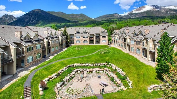 A residential complex with multiple two-story houses, a central courtyard with a circular stone pattern, and a mountainous backdrop.