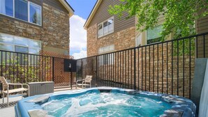 A hot tub with a stone wall backdrop, a wooden deck, and a metal fence.