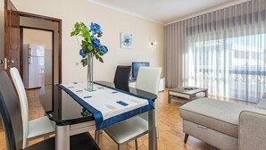 A modern living room with a dining area, a sofa, a coffee table, and a large window with curtains. - Seaside Charm in Gale - 2 Bedroom W/big Terrace (Albufeira)