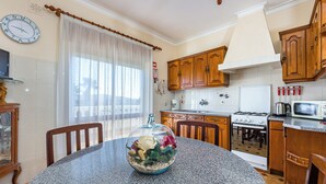 A kitchen with granite countertops, wooden cabinets, a stove, and a dining area with a table and chairs. - Seaside Charm in Gale - 2 Bedroom W/big Terrace (Albufeira)