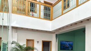 A spacious indoor area with multiple tables and chairs, a green wall with a painting, and a wooden balcony with decorative railings. - Riad Madinina (Marrakech)