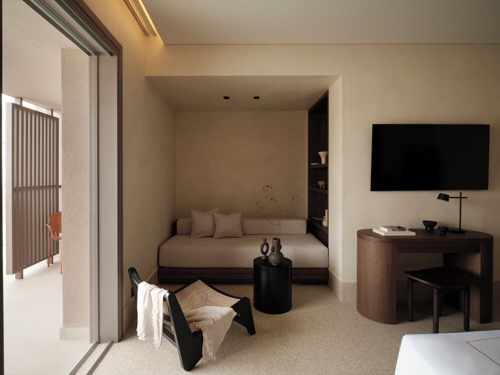 A modern hotel room with a sofa bed, a small desk, a TV, and a chair.