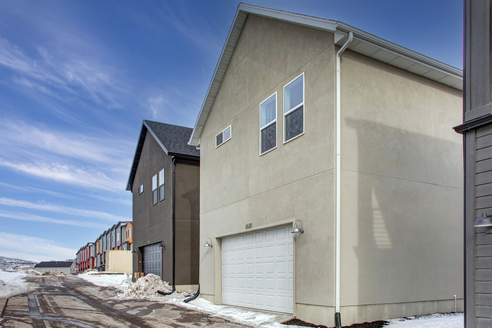 A modern residential building with a garage, a driveway, and a snow-covered ground.