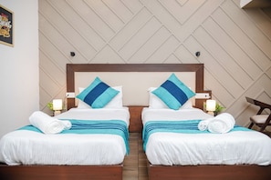 A hotel room with two beds, each with white bedding and blue accents, a wooden headboard, and a wall-mounted light fixture. - 26 Vamsor Heights (Gurugram)