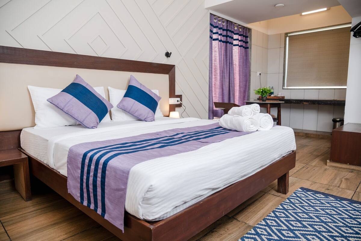 A neatly made bed with white and blue bedding, a wooden headboard, and a blue patterned rug.