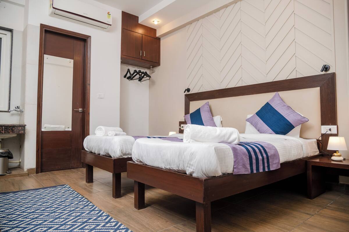A hotel room with a large bed, a wooden headboard, a bedside table with a lamp, and a blue patterned rug.