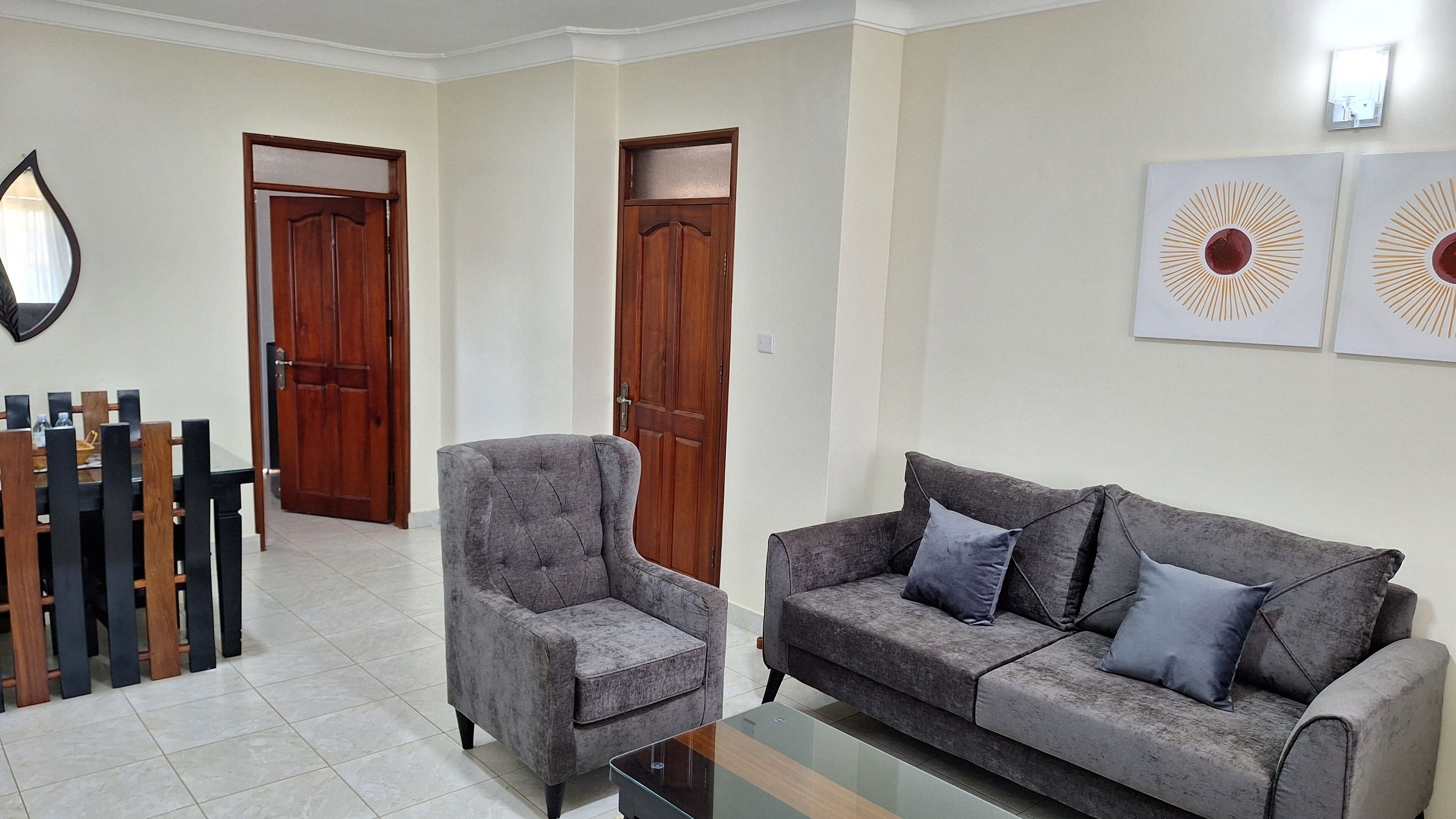 Una sala de estar con un sofá gris, un sillón a juego y una mesa de centro. Hay dos puertas de madera y un espejo en la pared.