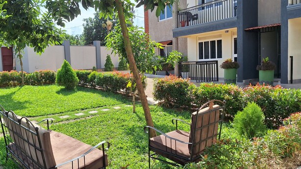 A courtyard with a lawn, two benches, and a building with balconies. - Oreville Apartments Namugongo Seeta Rd (Seeta)