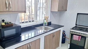 A modern kitchen with a black countertop, stainless steel appliances, and wooden cabinets. - Oreville Apartments Namugongo Seeta Rd (Seeta)