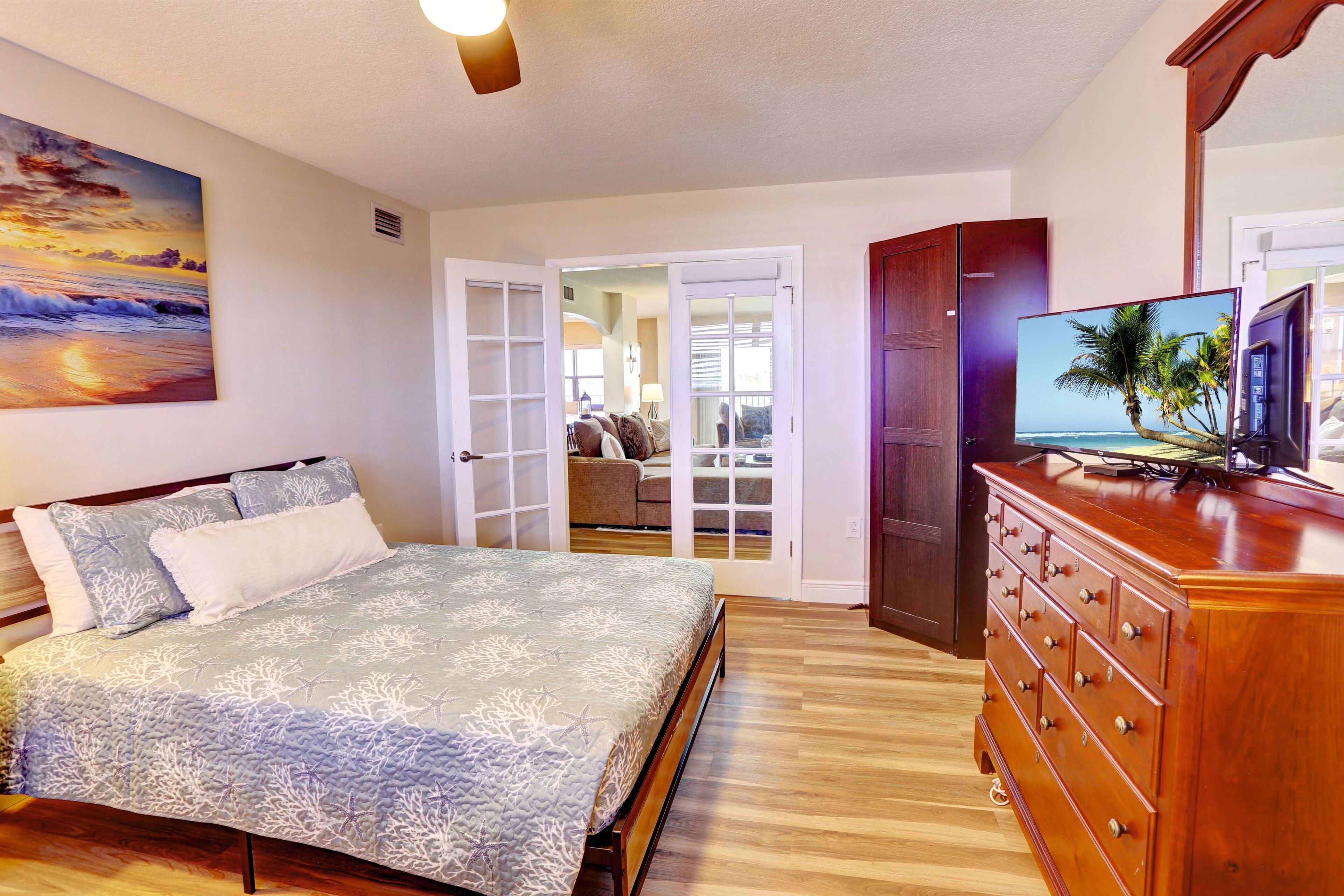 Een slaapkamer met een bed, een dressoir, een televisie en een schilderij van een zonsondergang.
