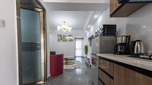 A modern kitchen with a microwave, coffee maker, and kettle. There is a red chair and a plant in the dining area. - Erica Suites - Riverside 1BR Apartments (Nairobi)