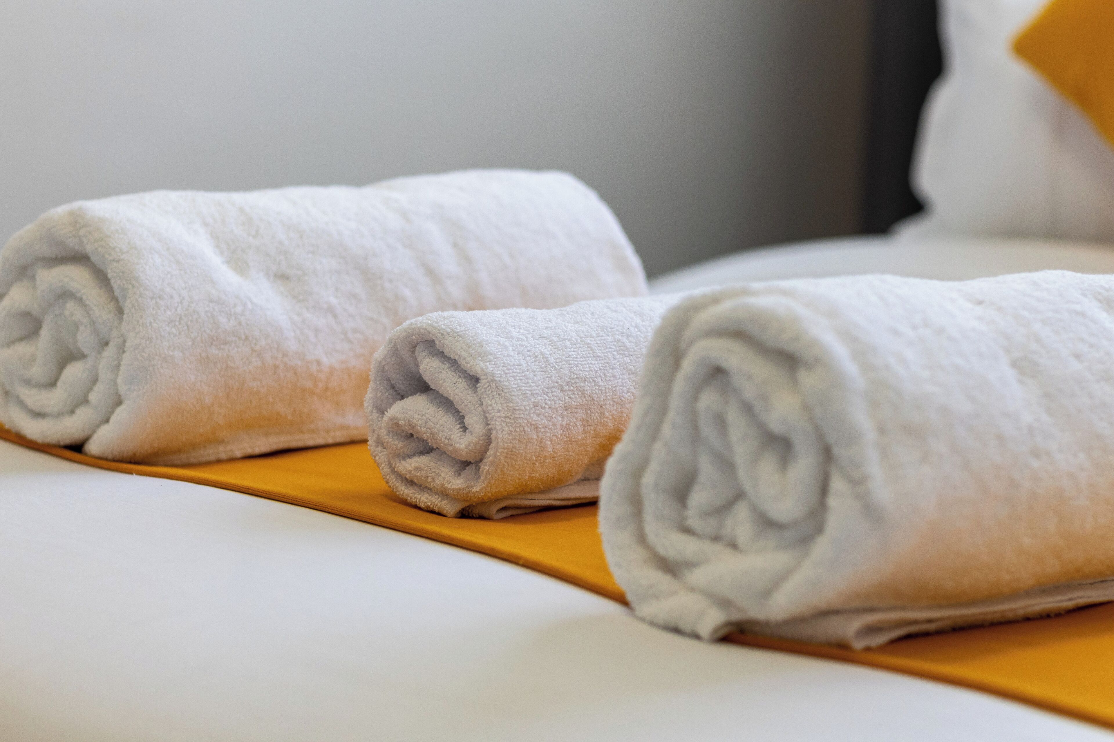 Una cama bien hecha con dos toallas blancas enrolladas sobre una bandeja amarilla.