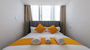 A neatly made bed with white and yellow bedding, two pillows, and rolled towels. - Erica Suites - Riverside 1BR Apartments (Nairobi)