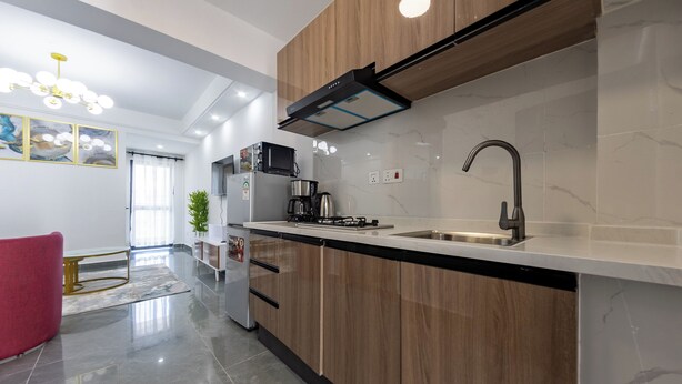 A modern kitchen with wooden cabinets, a stainless steel sink, and a built-in range hood. - Erica Suites - Riverside 1BR Apartments (Nairobi)