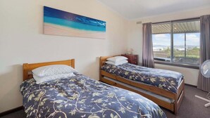 Un dormitorio con dos camas, un cuadro de una playa, una ventana con vistas y un ventilador de techo.