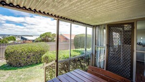 Un espacio exterior cubierto con un banco de madera, ventanas amplias y vistas del paisaje circundante.