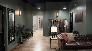 A modern living room with a leather sofa, a coffee table, and a lamp. There is a hallway leading to a kitchen and a dining area. - Luxury 6,000+ sq ft Hideaway with Heated Pool, Spa, & Sauna - near Greenville (Taylors)