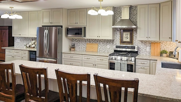 A modern kitchen with white cabinets, stainless steel appliances, a large island with bar stools, and pendant lighting. - Luxury 6,000+ sq ft Hideaway with Heated Pool, Spa, & Sauna - near Greenville (Taylors)