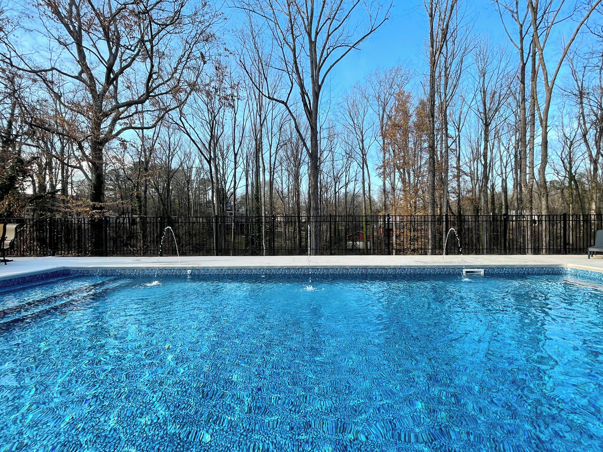 Une piscine à l’eau d’un bleu cristallin, entourée d’une clôture en métal noir et d’arbres.