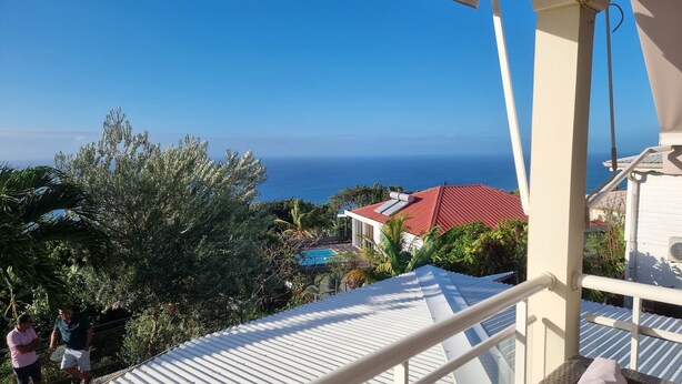 A balcony with a view of the ocean and a red-roofed building.