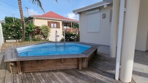 A wooden deck with a hot tub, surrounded by a house with a red roof and a white exterior wall.