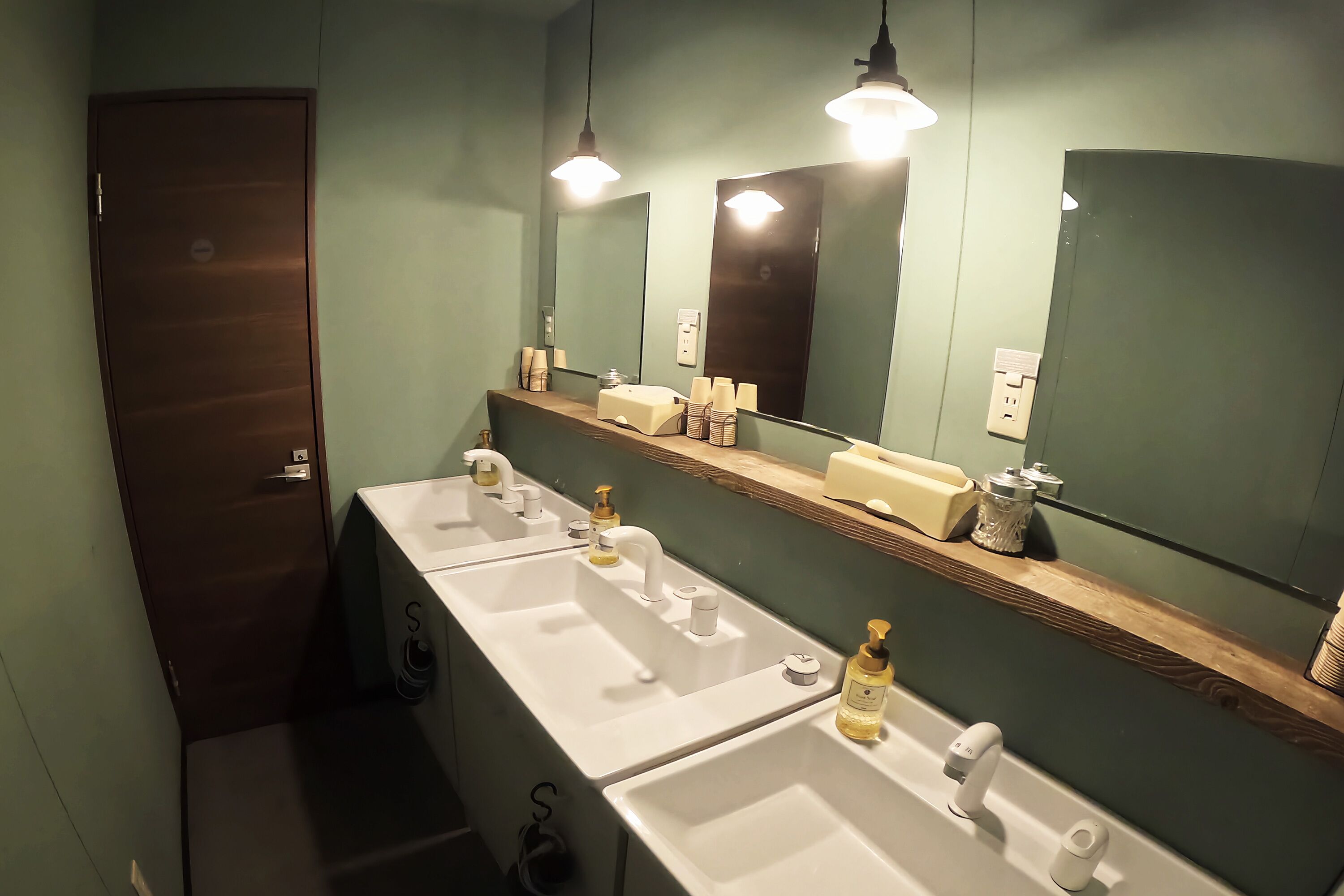 A bathroom with three sinks, a mirror, and a wooden shelf with toiletries.