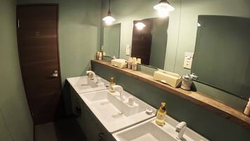 A bathroom with three sinks, a mirror, and a wooden shelf with toiletries.