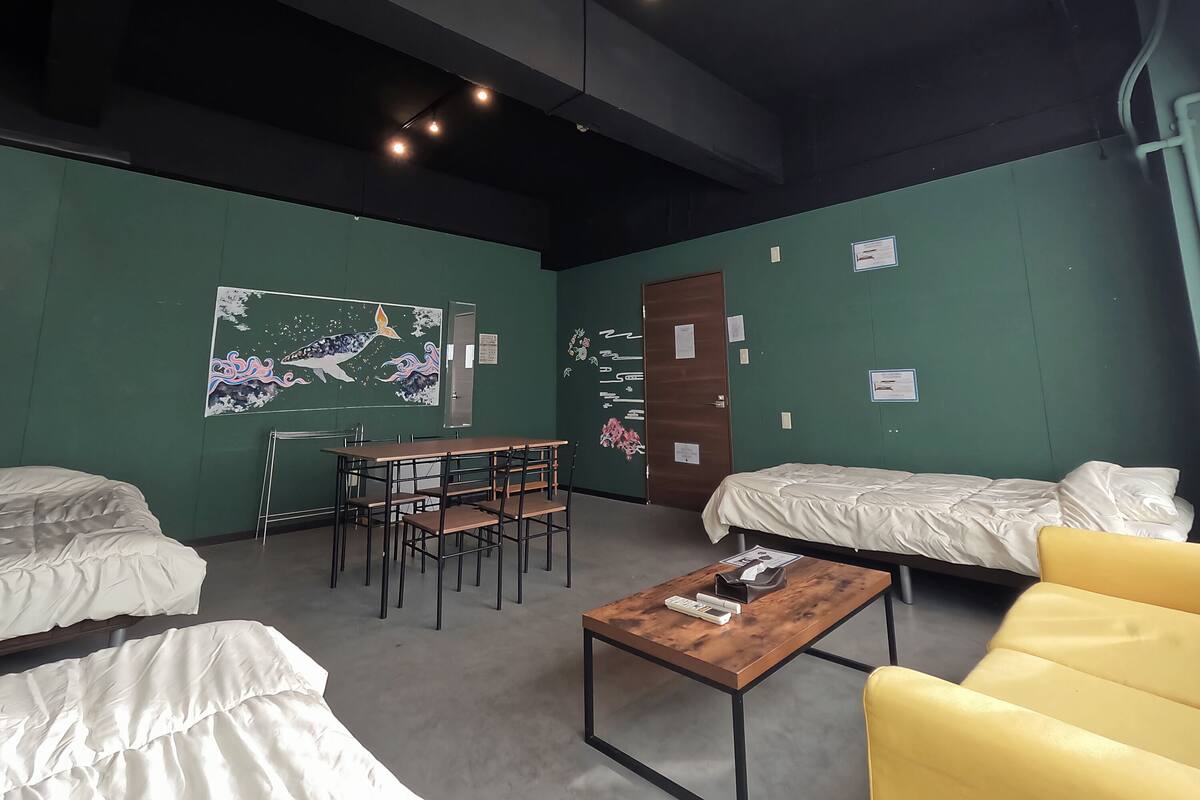 A room with two beds, a table, chairs, and a painting on the wall.
