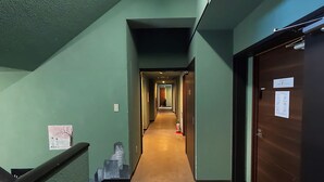 A hallway with green walls, a wooden door on the right, and a fire extinguisher on the floor. - TASOGARE HOSTEL (Hakodate)
