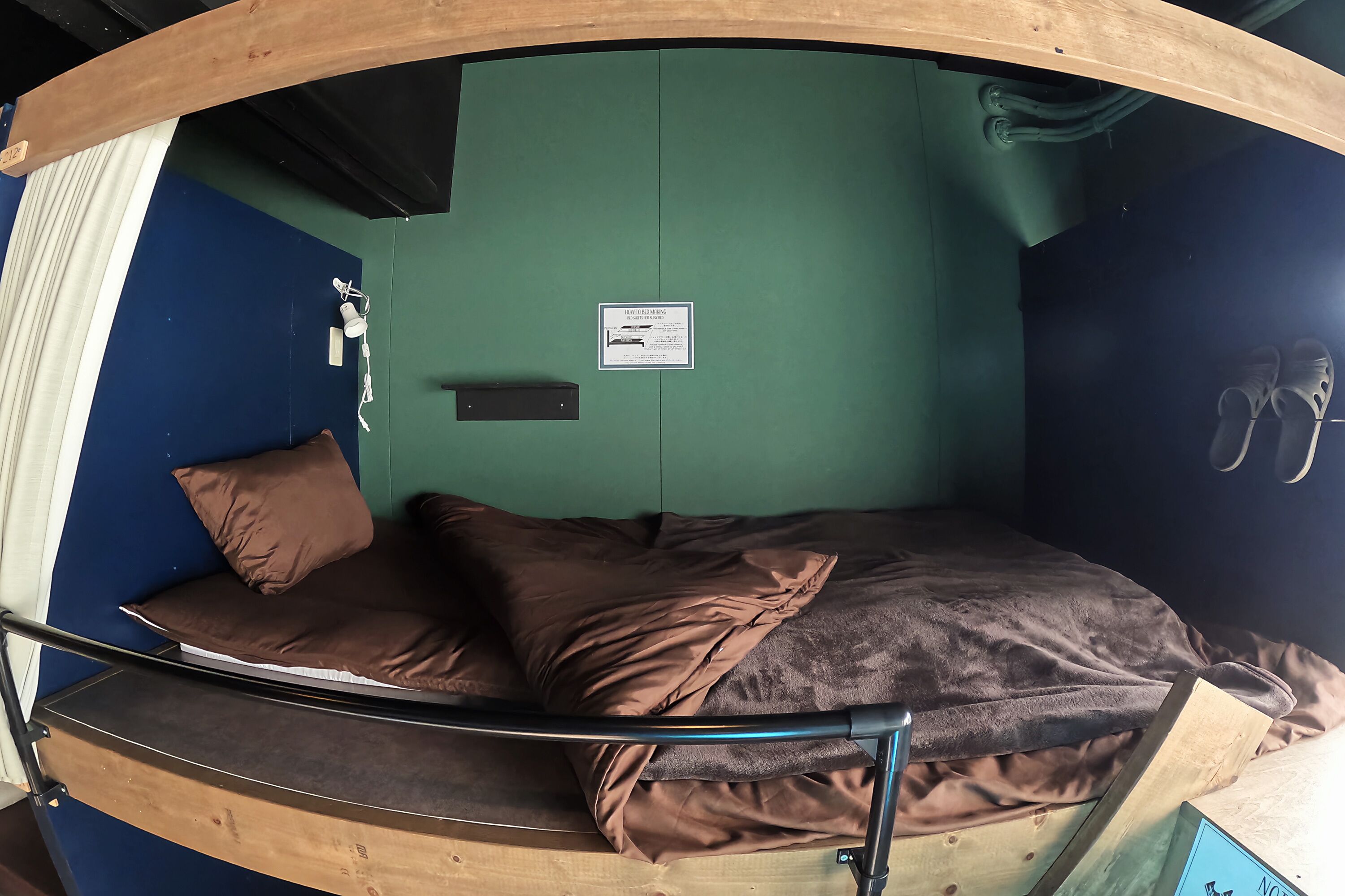 A bunk bed with a mattress and pillows, a metal frame, a green wall, a small sign, and a pair of shoes hanging on the wall.