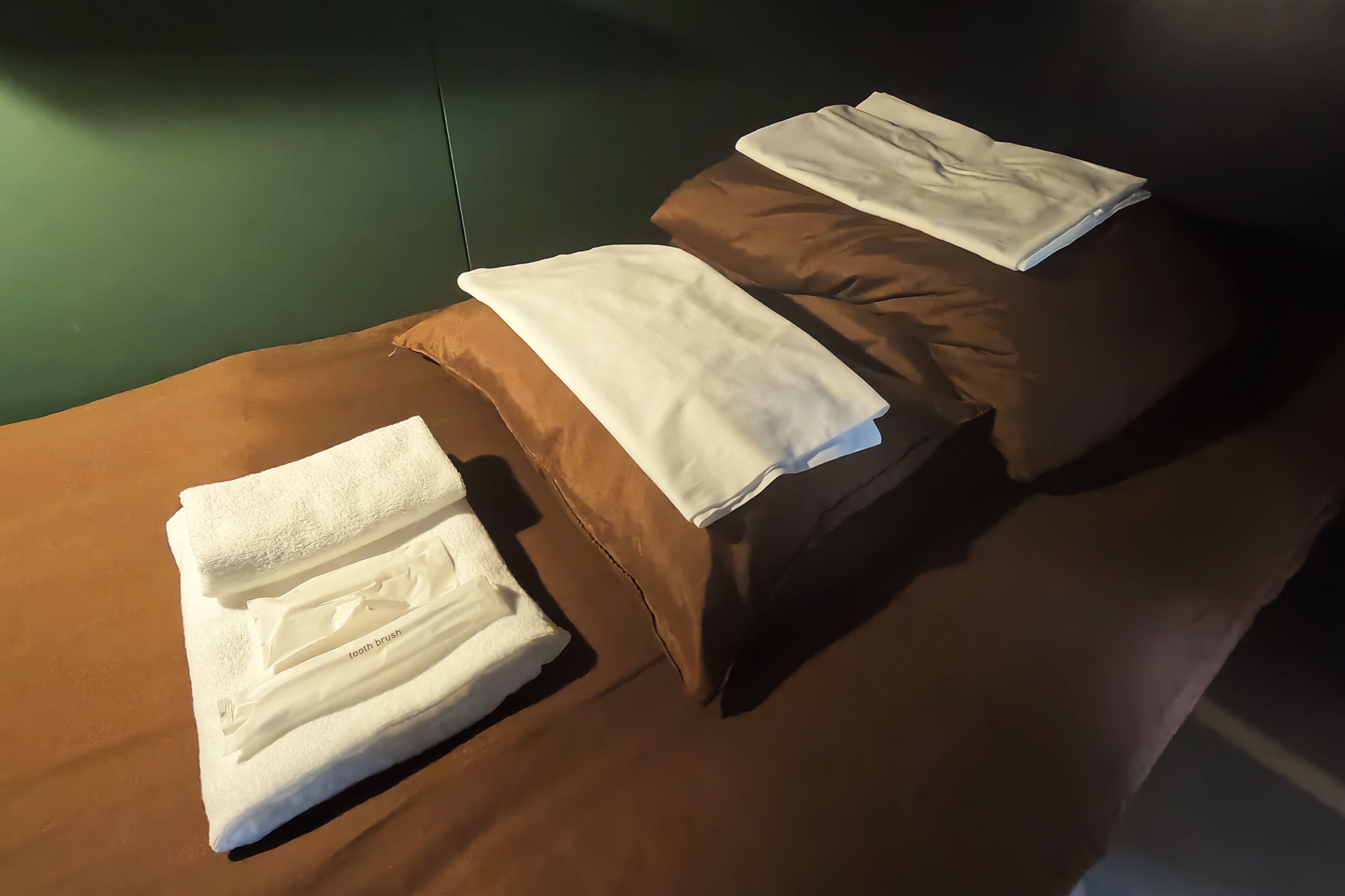Letto rifatto con biancheria marrone e asciugamani bianchi ripiegati sopra.