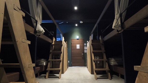 A narrow hallway with bunk beds and wooden ladders, leading to a door at the end. - TASOGARE HOSTEL (Hakodate)