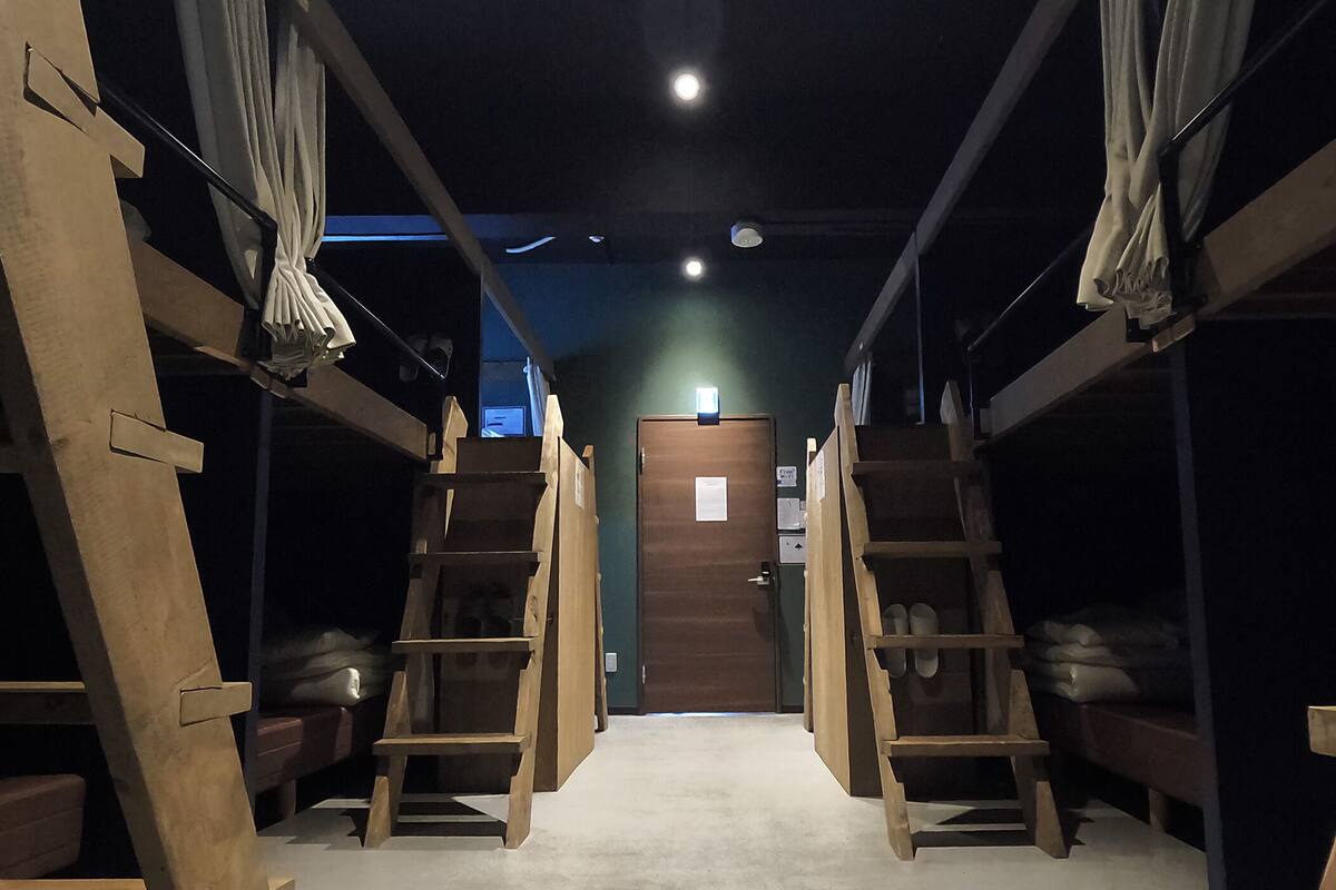 A narrow hallway with bunk beds and wooden ladders, leading to a door at the end.