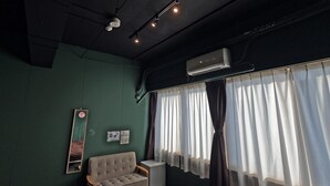 A room with a green wall, a sofa, a small table, a mirror, and a window with curtains. - TASOGARE HOSTEL (Hakodate)