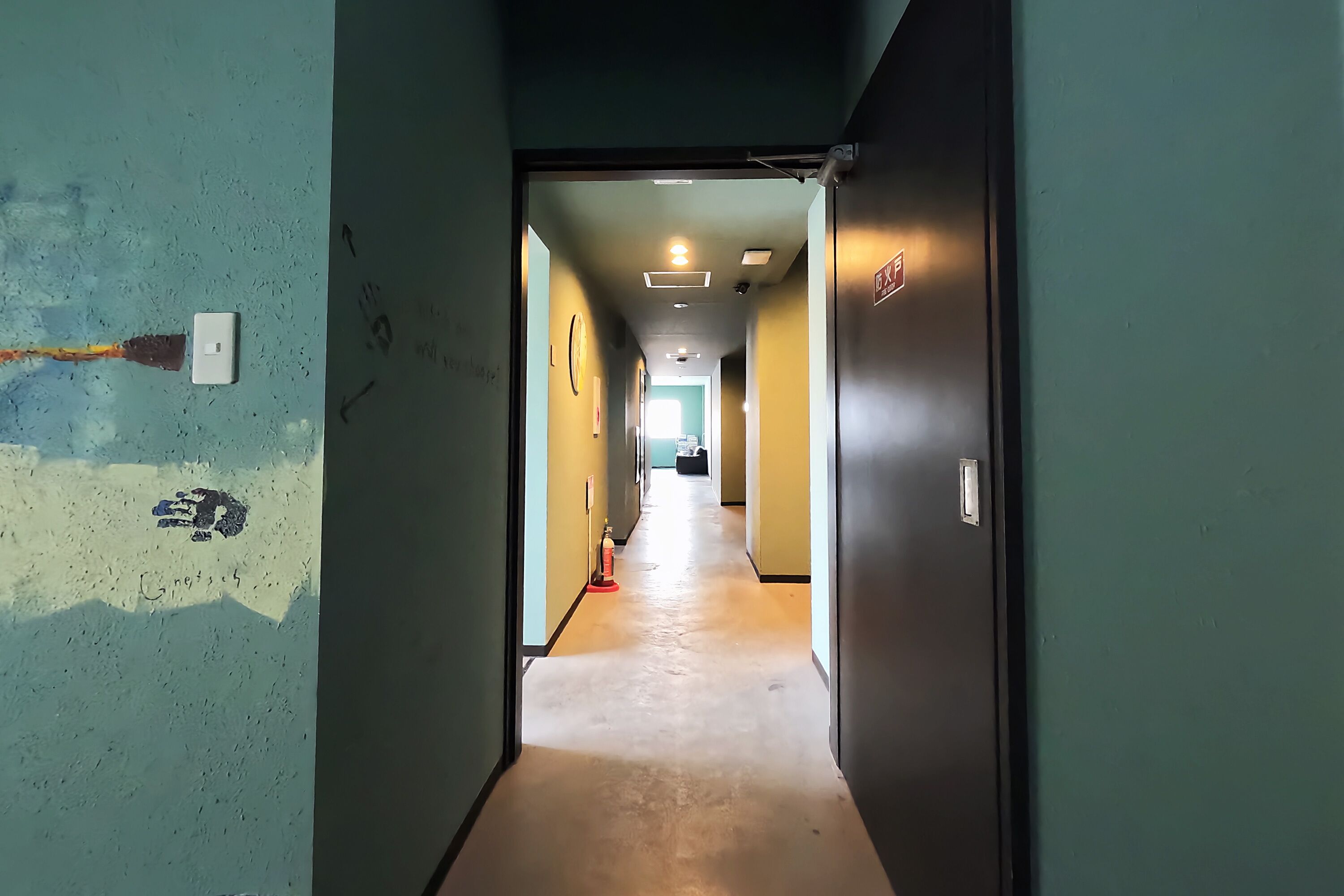 Un pasillo con piso de color claro, una puerta a la derecha e interruptor de luz en la pared.