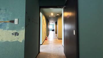 Un pasillo con piso de color claro, una puerta a la derecha e interruptor de luz en la pared.