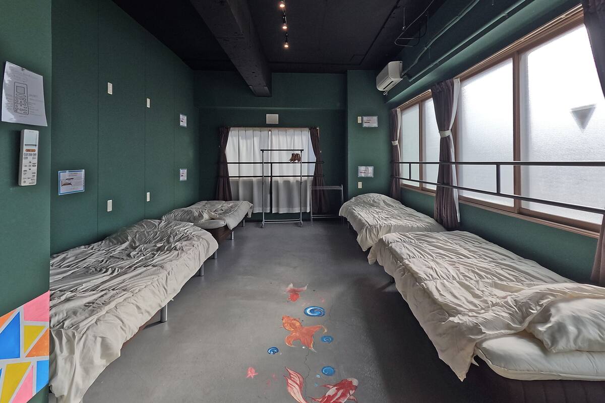A room with two single beds, a window with curtains, and a wall-mounted air conditioner.